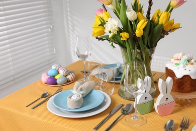Photo of Festive table setting with painted eggs, traditional Easter cake and vase of tulips