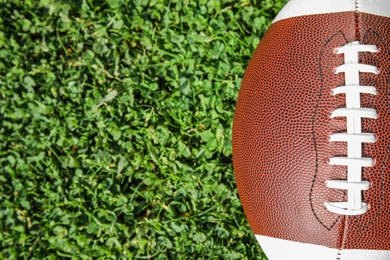 Photo of Ball for American football on fresh green field grass, top view. Space for text
