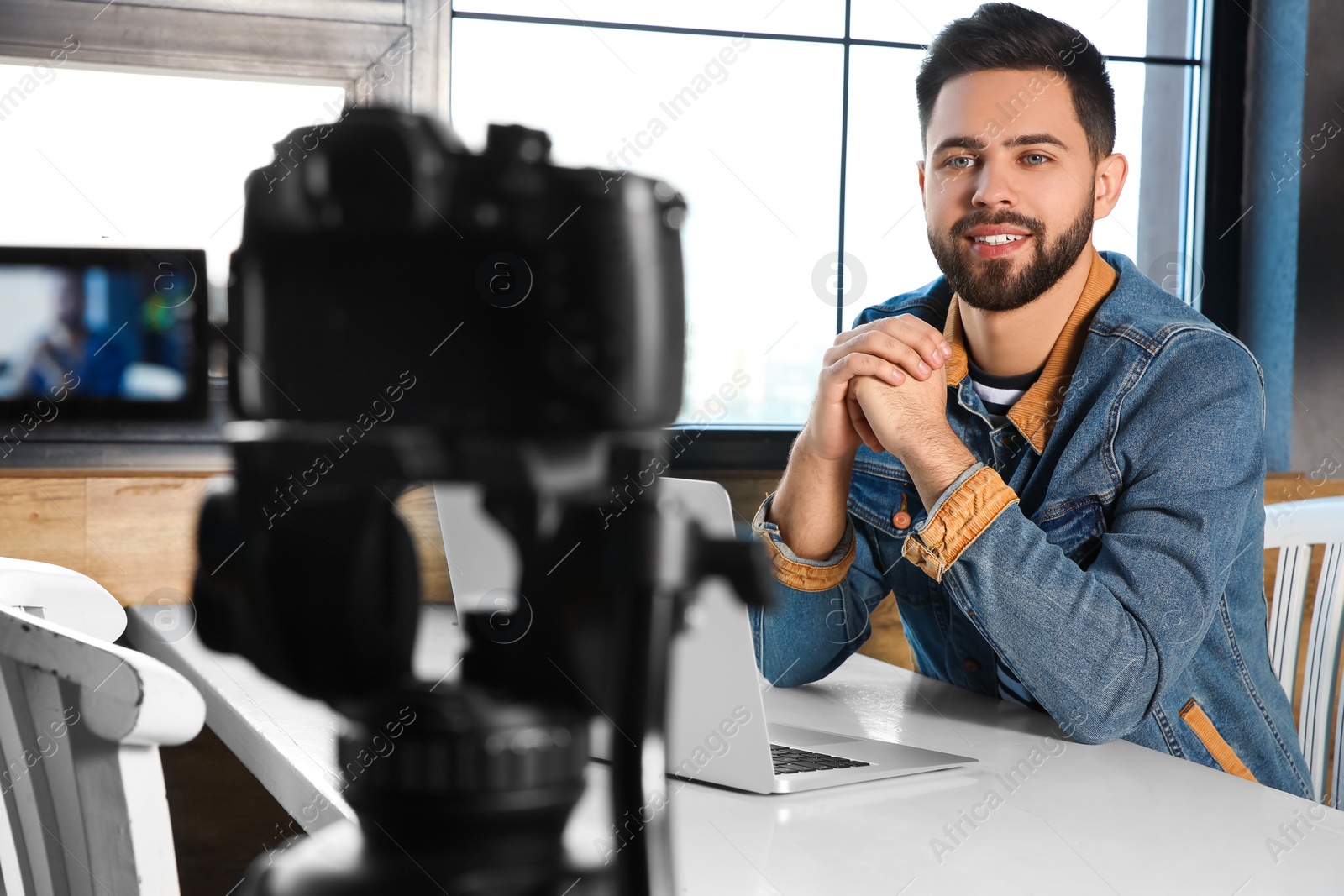 Photo of Young blogger with laptop recording video on camera at cafe