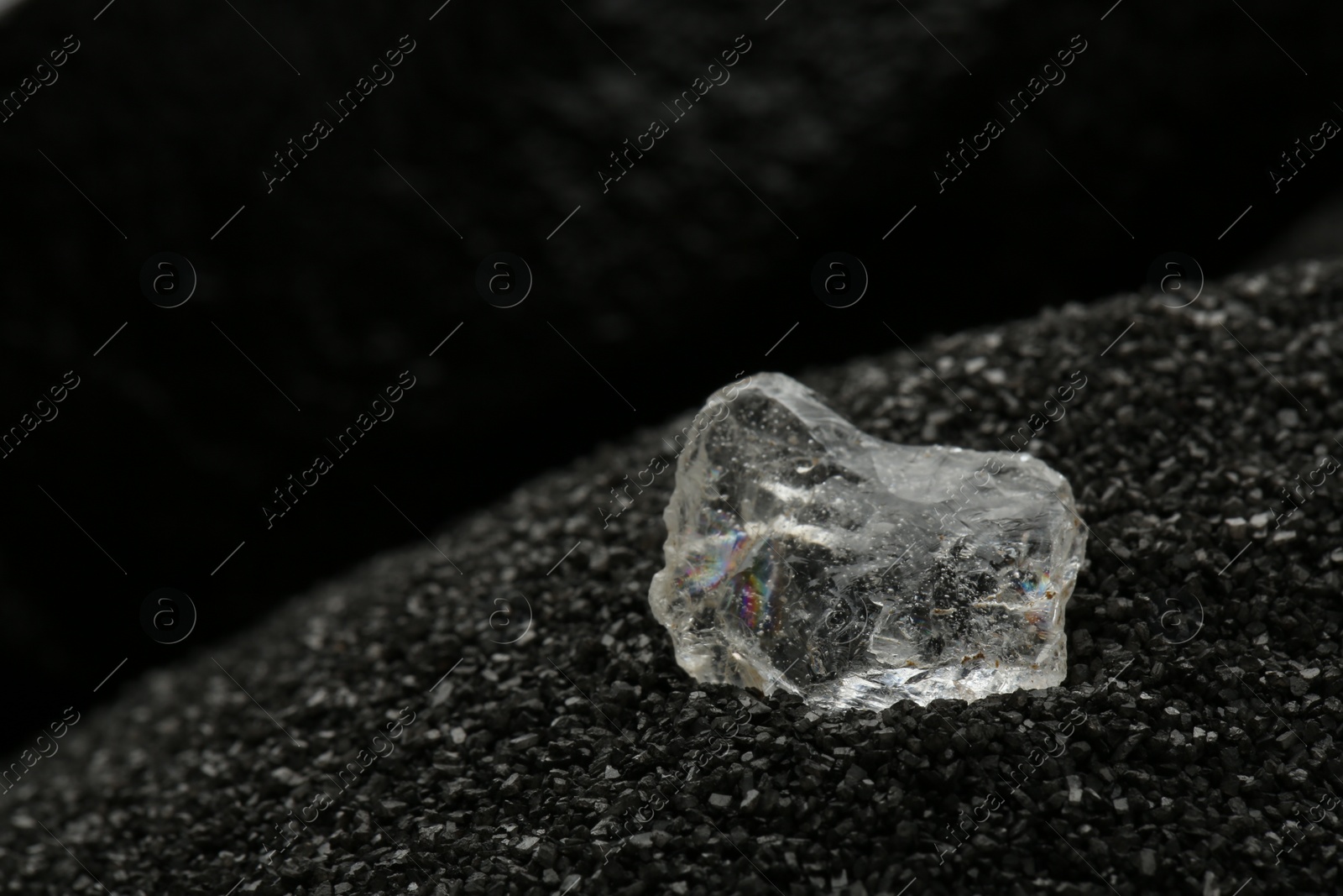 Photo of Shiny rough diamond on decorative black sand, closeup. Space for text