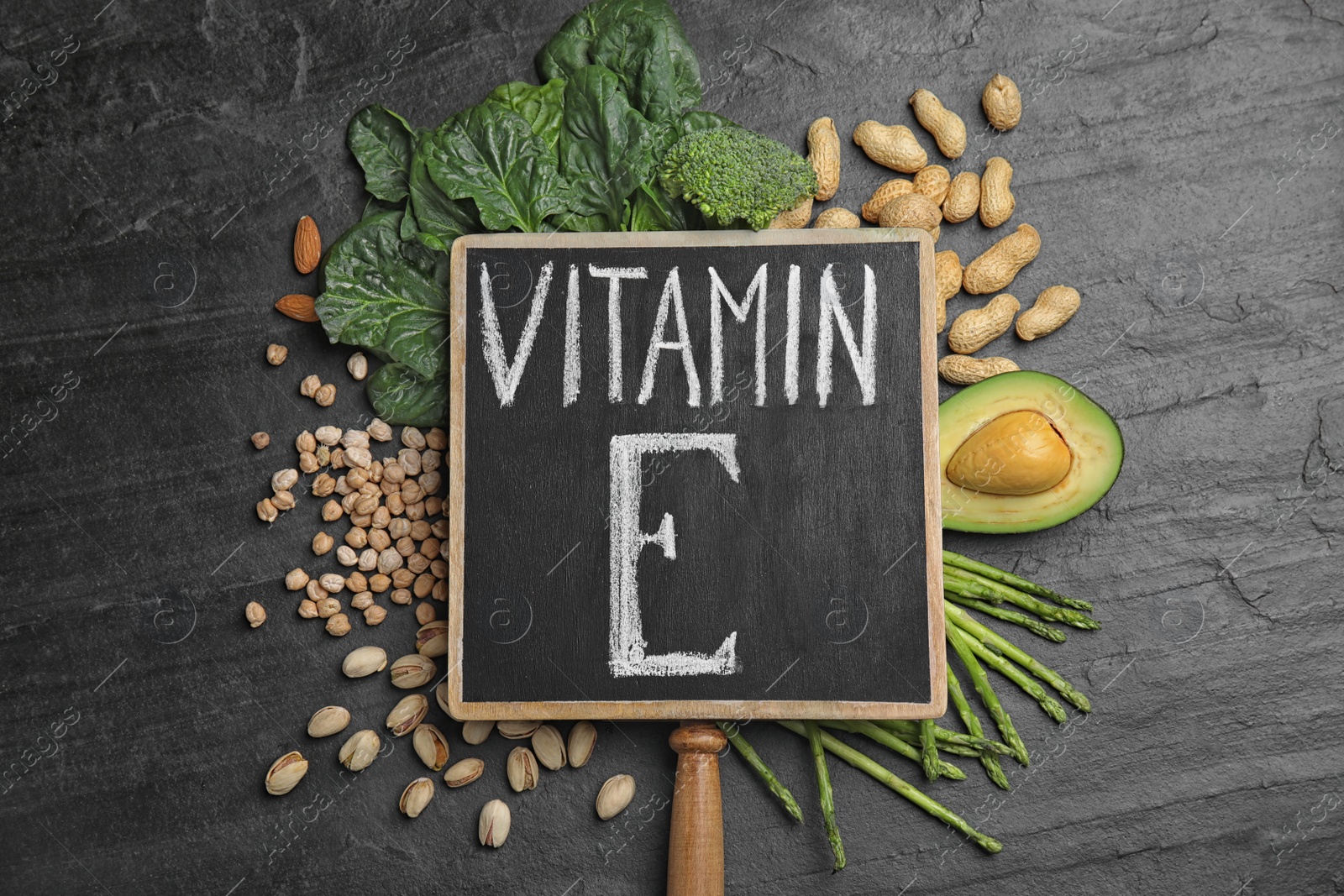 Photo of Small chalkboard with phrase Vitamin E and different products on dark background, flat lay