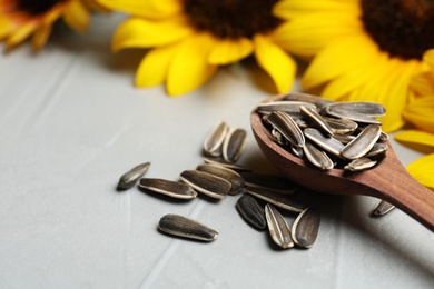 Raw sunflower seeds and flowers on grey table, closeup. Space for text