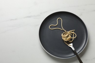 Heart made of tasty spaghetti and fork on white marble table, top view. Space for text