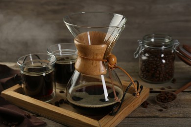 Photo of Glass chemex coffeemaker with coffee and beans on wooden table, closeup