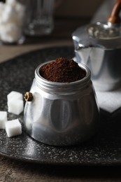 Ground coffee in moka pot and sugar cubes on wooden table, closeup