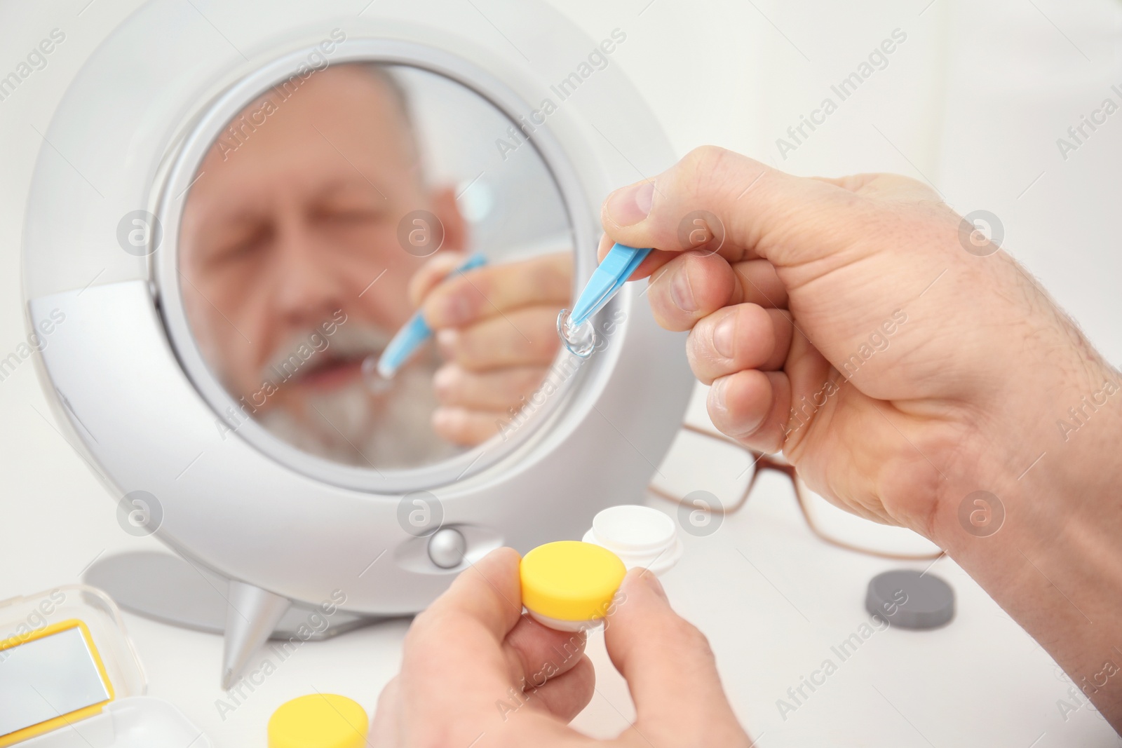 Photo of Senior man taking contact lens from container in front of mirror