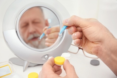 Photo of Senior man taking contact lens from container in front of mirror