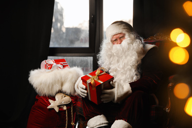 Santa Claus with Christmas gifts in armchair near window indoors