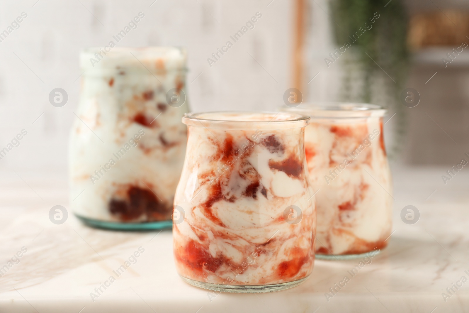 Photo of Tasty yoghurt with jam on white marble board, closeup