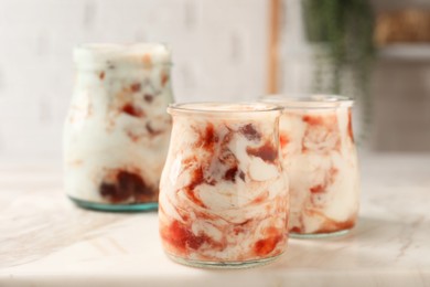 Photo of Tasty yoghurt with jam on white marble board, closeup