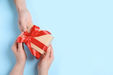 Photo of Man giving gift box to woman on light blue background, top view. Space for text