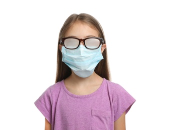 Photo of Little girl with foggy glasses caused by wearing disposable mask on white background. Protective measure during coronavirus pandemic