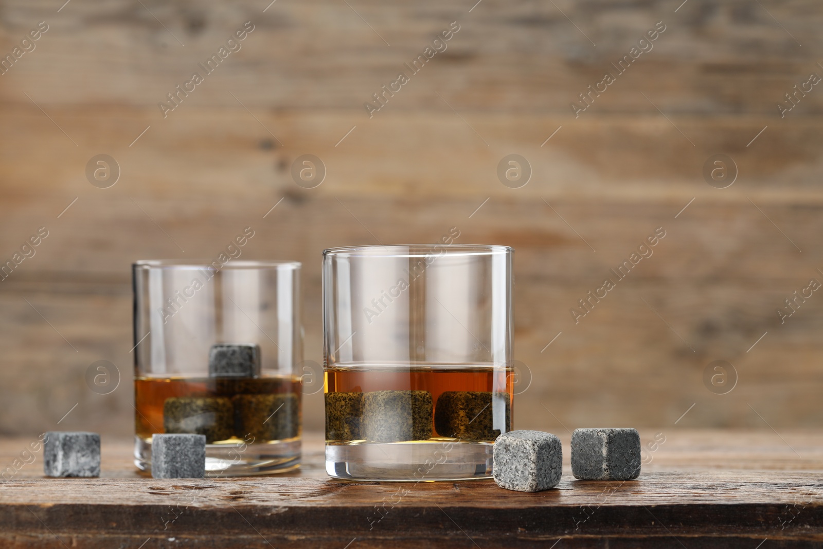 Photo of Whiskey stones and drink in glasses on wooden table, closeup. Space for text