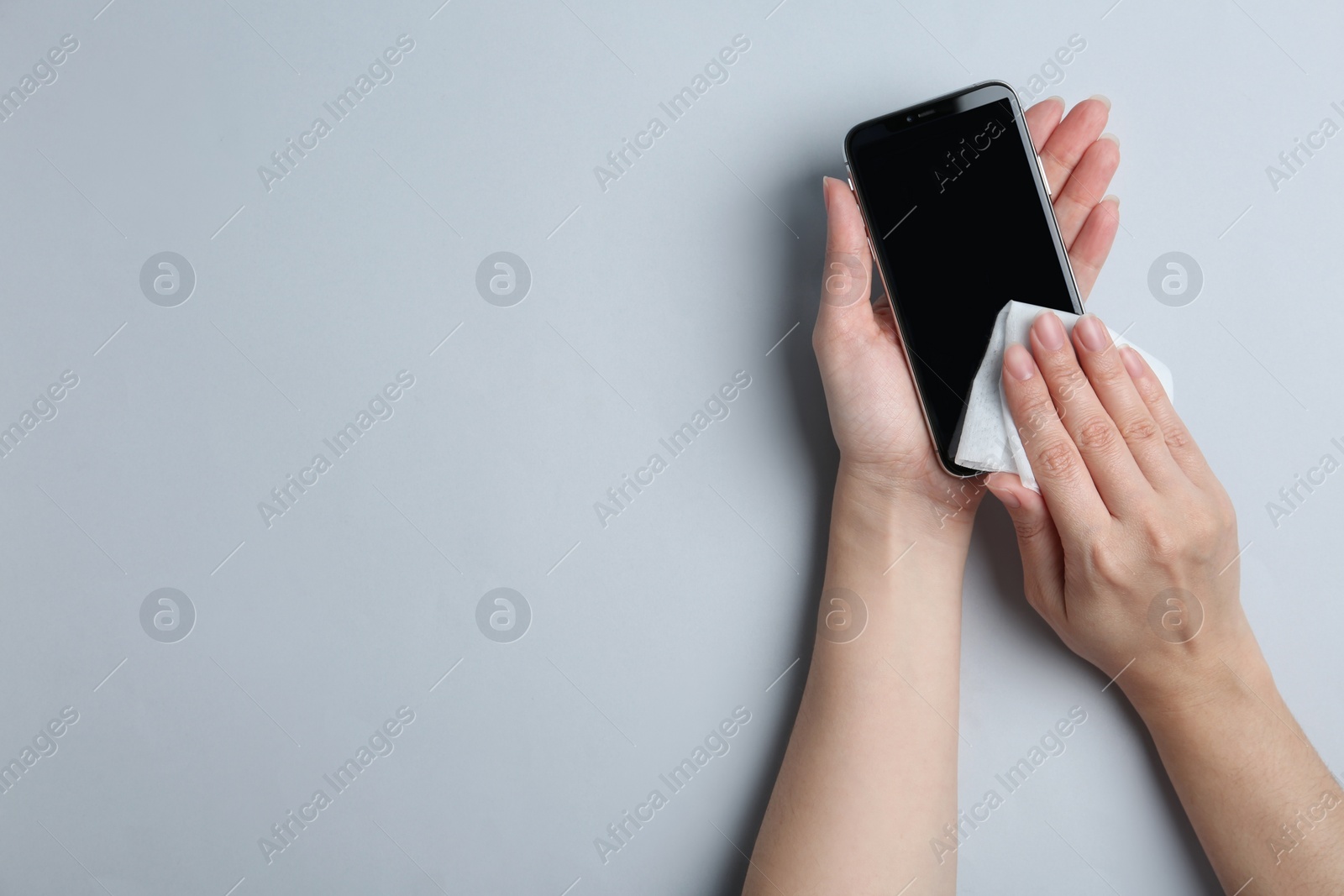 Photo of Woman cleaning mobile phone with antiseptic wipe on light grey background, top view. Space for text