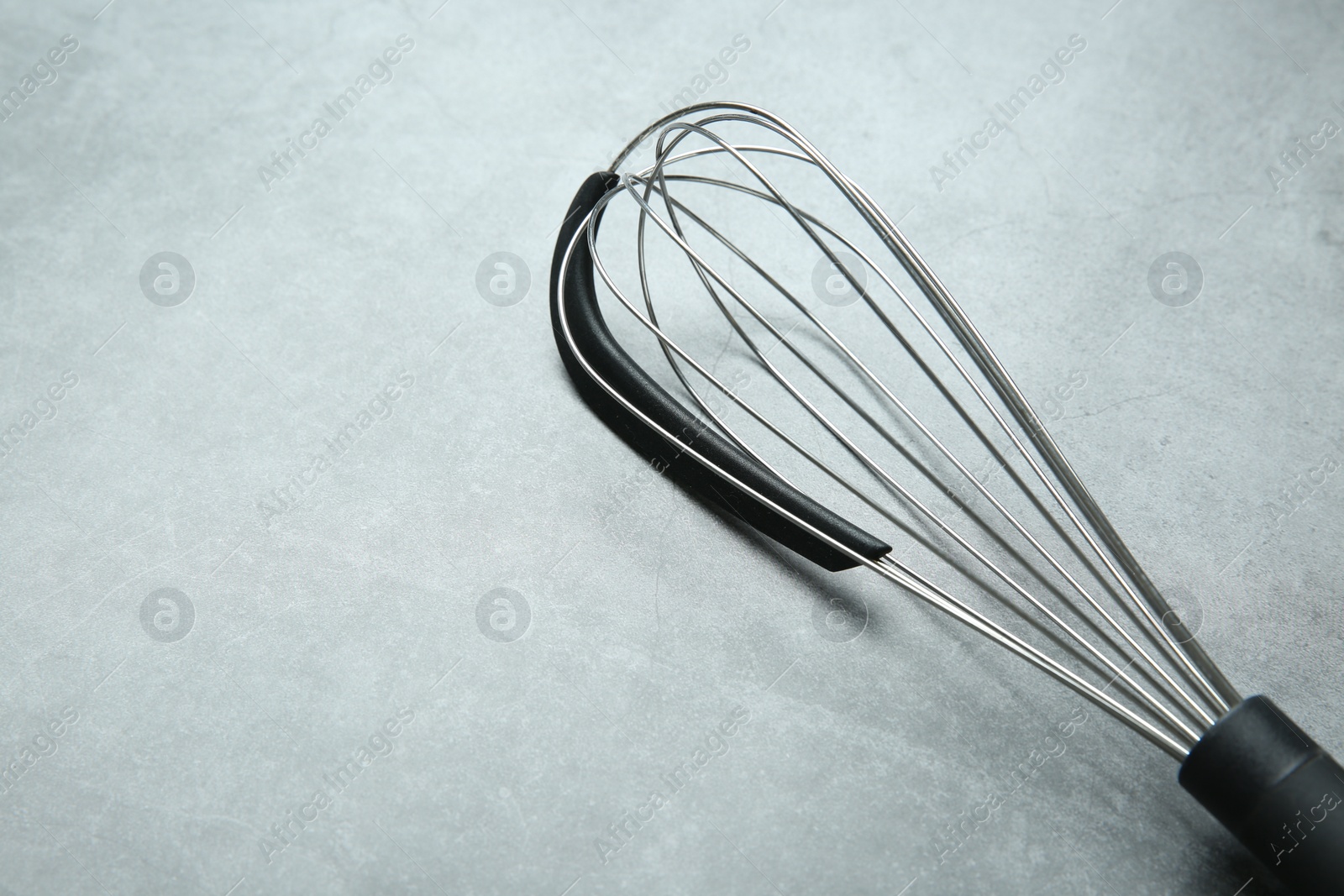 Photo of Metal whisk on gray table, space for text