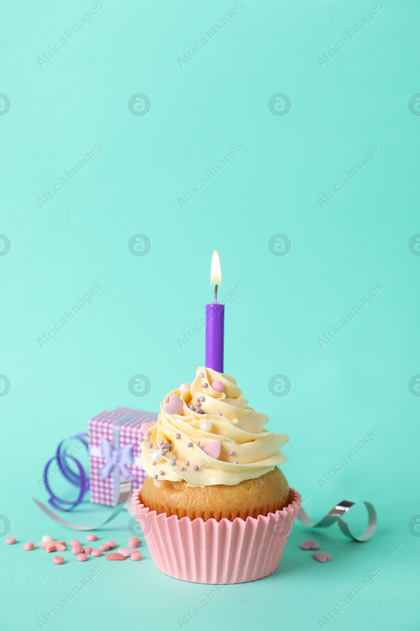 Photo of Birthday cupcake with burning candle, gift box  and sprinkles on turquoise background
