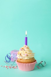 Photo of Birthday cupcake with burning candle, gift box  and sprinkles on turquoise background