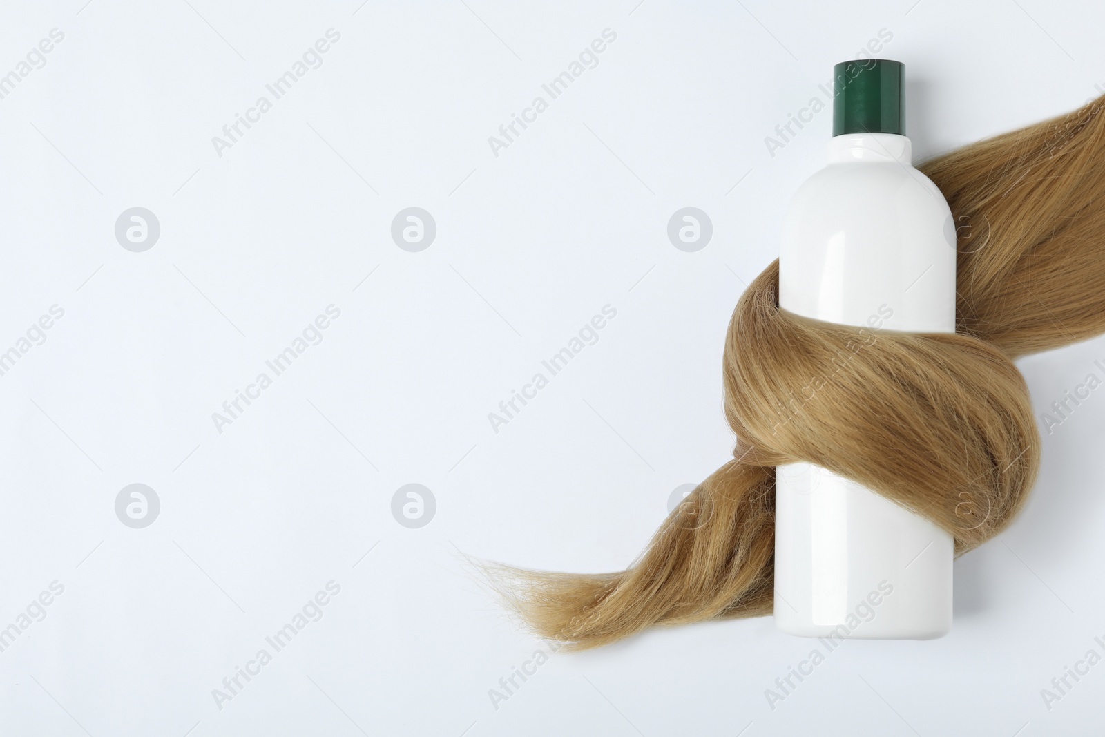 Photo of Shampoo bottle wrapped in lock of hair isolated on white, top view. Natural cosmetic products