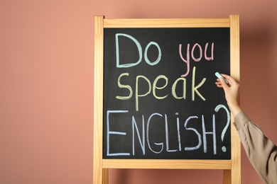 Photo of Woman writing question Do You Speak English on blackboard against pink background, closeup