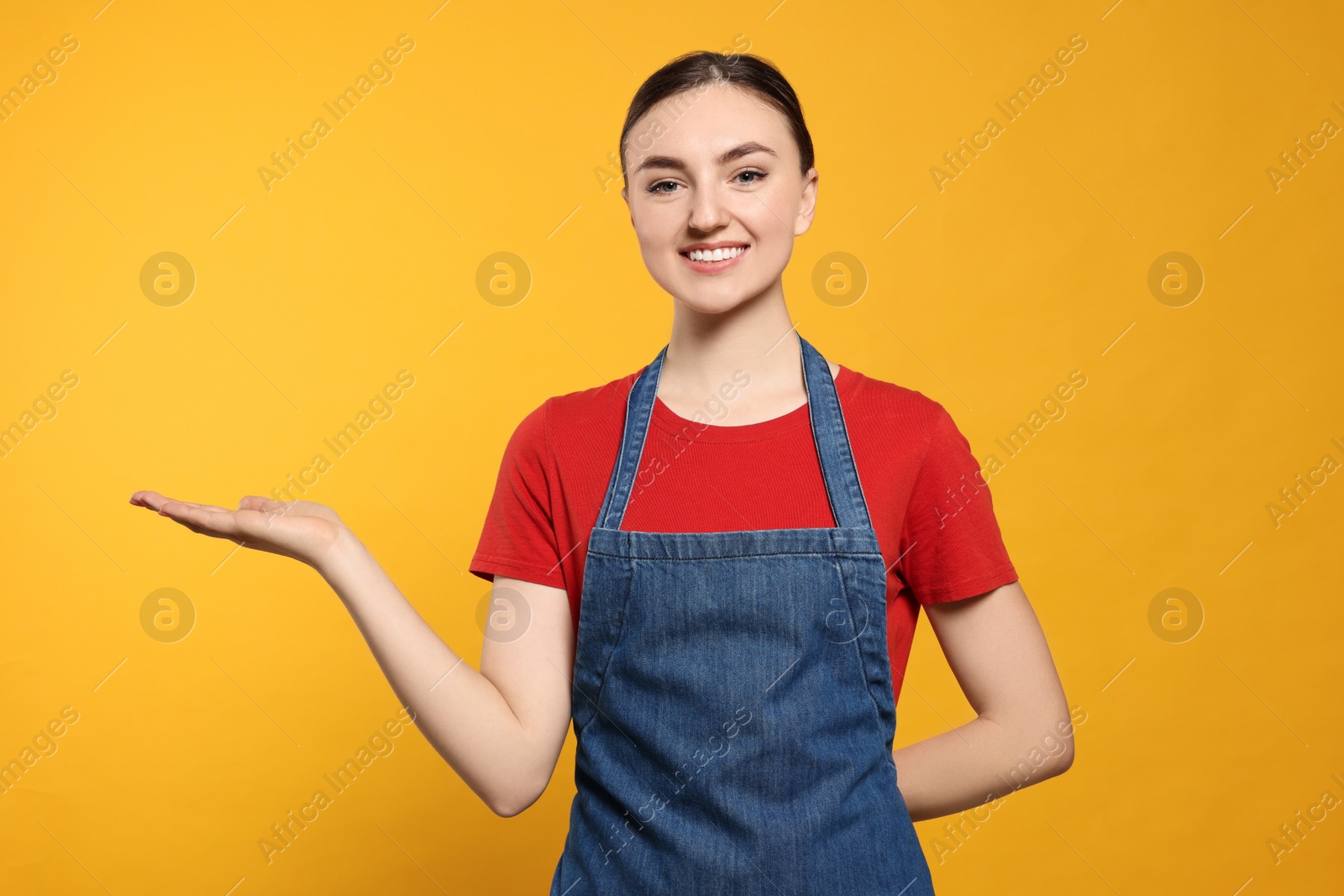 Photo of Beautiful young woman in clean denim apron on orange background