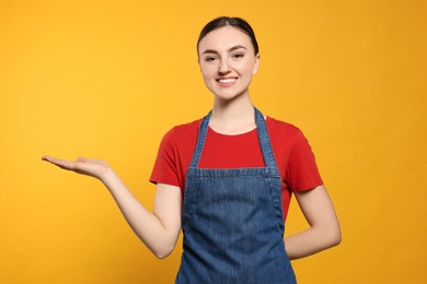 Beautiful young woman in clean denim apron on orange background