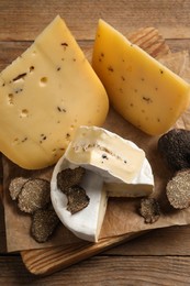 Photo of Board with delicious cheeses and fresh black truffles on wooden table, top view