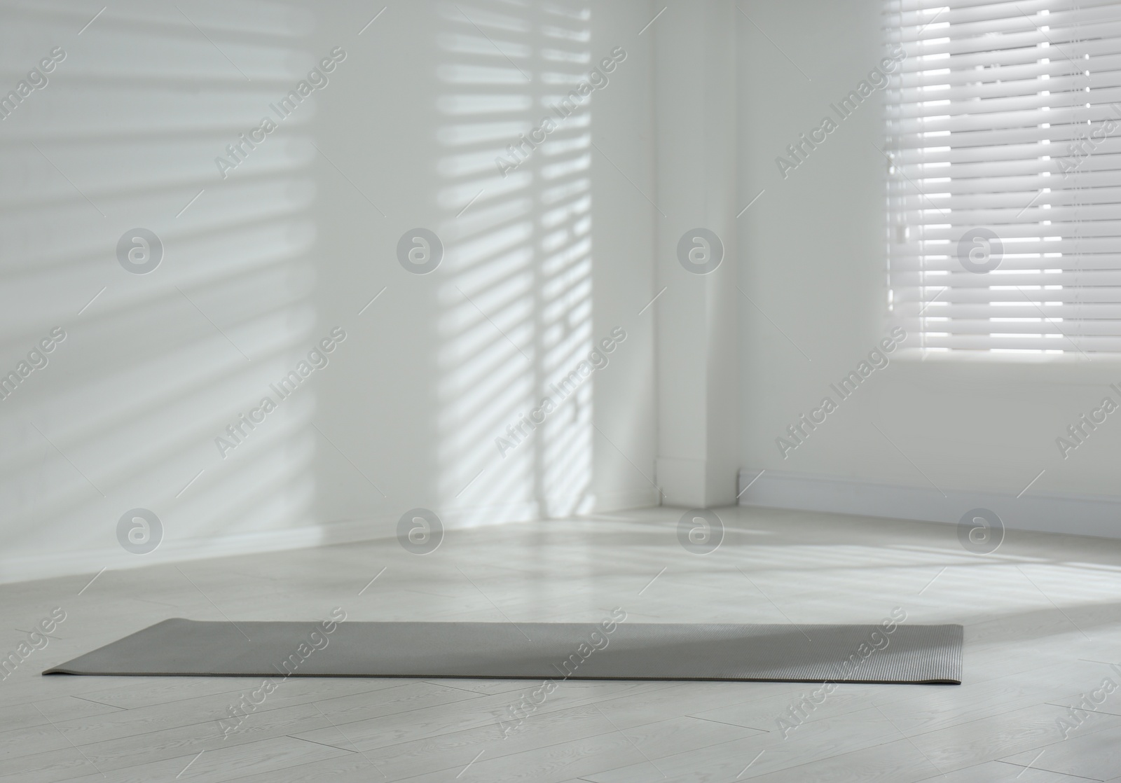 Photo of Unrolled grey yoga mat on floor in room. Space for text