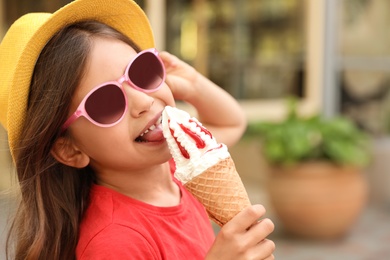 Cute little girl with delicious ice cream in park, space for text