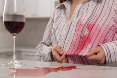 Woman with spilled wine over her shirt and marble table in kitchen, closeup