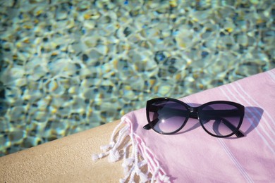 Stylish sunglasses and blanket near outdoor pool on sunny day, space for text