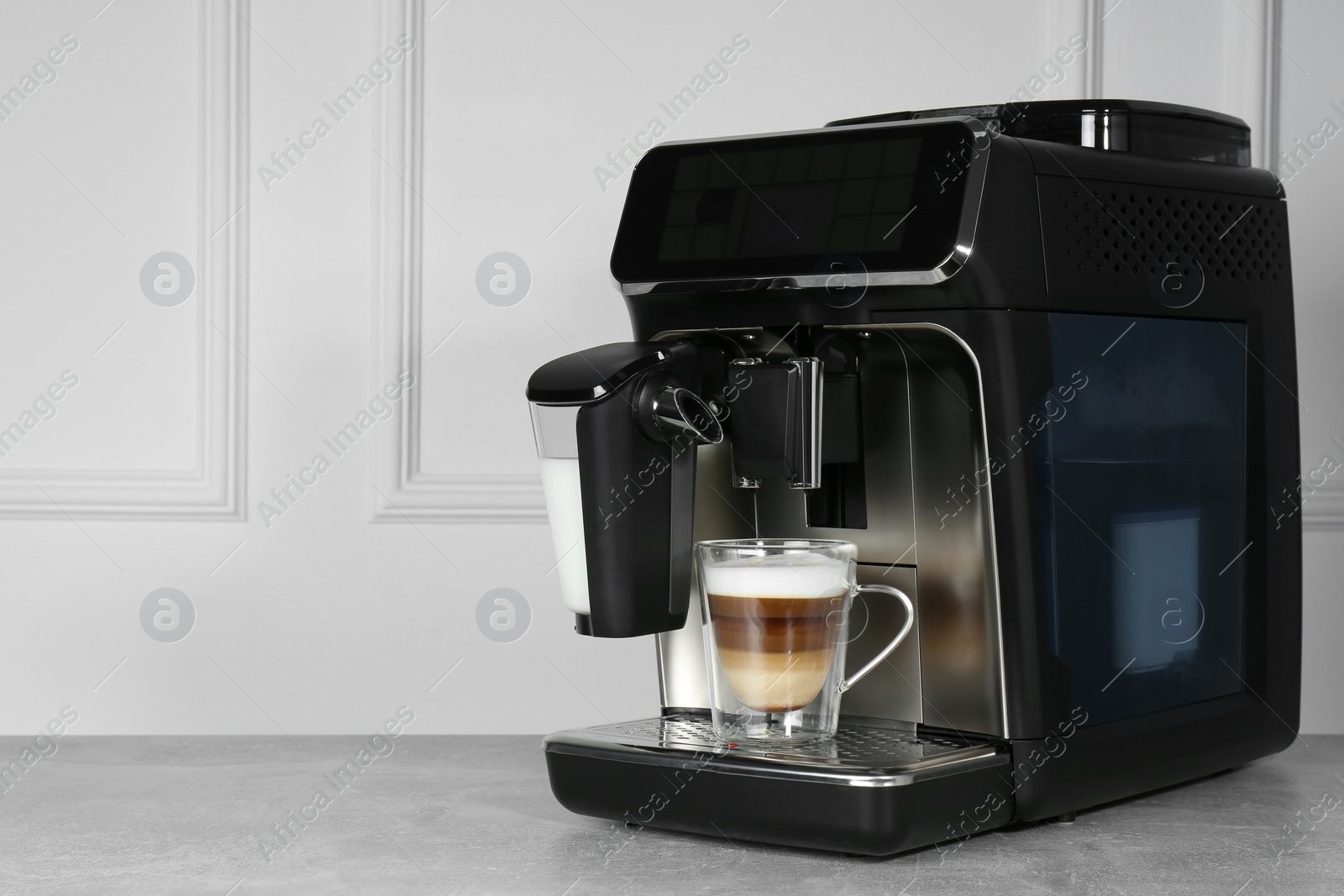 Photo of Modern coffee machine with glass cup of latte on grey table near white wall. Space for text