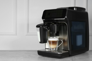 Photo of Modern coffee machine with glass cup of latte on grey table near white wall. Space for text