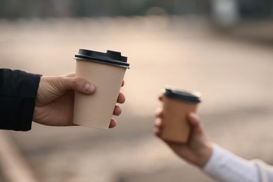 Man and woman holding paper coffee cups outdoors, closeup