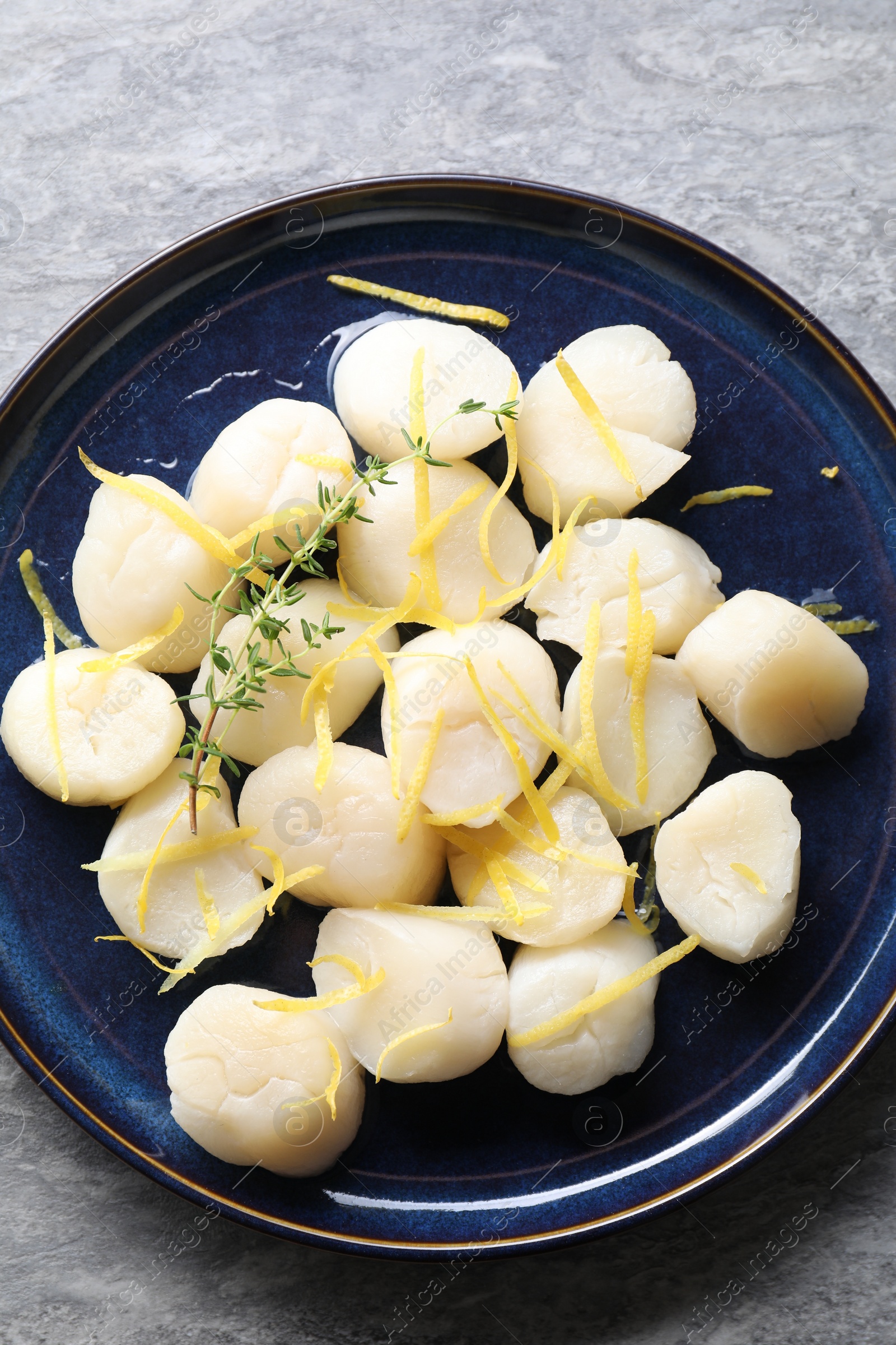 Photo of Raw scallops with thyme and lemon zest on grey marble table, top view