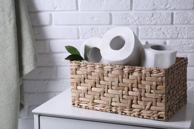 Photo of Toilet paper rolls in wicker basket and floral decor on chest of drawers near white brick wall