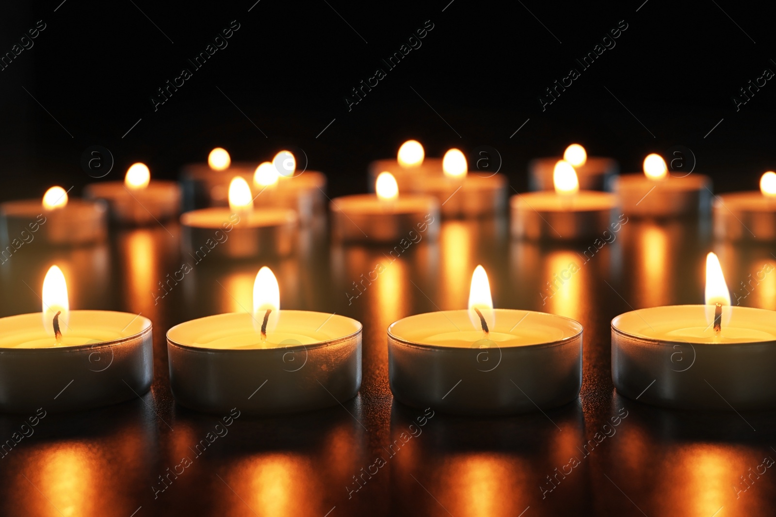 Photo of Wax candles burning on table in darkness, closeup