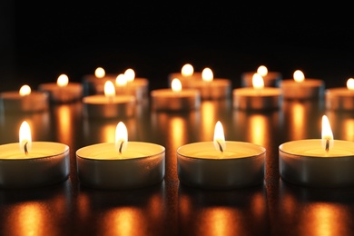 Photo of Wax candles burning on table in darkness, closeup