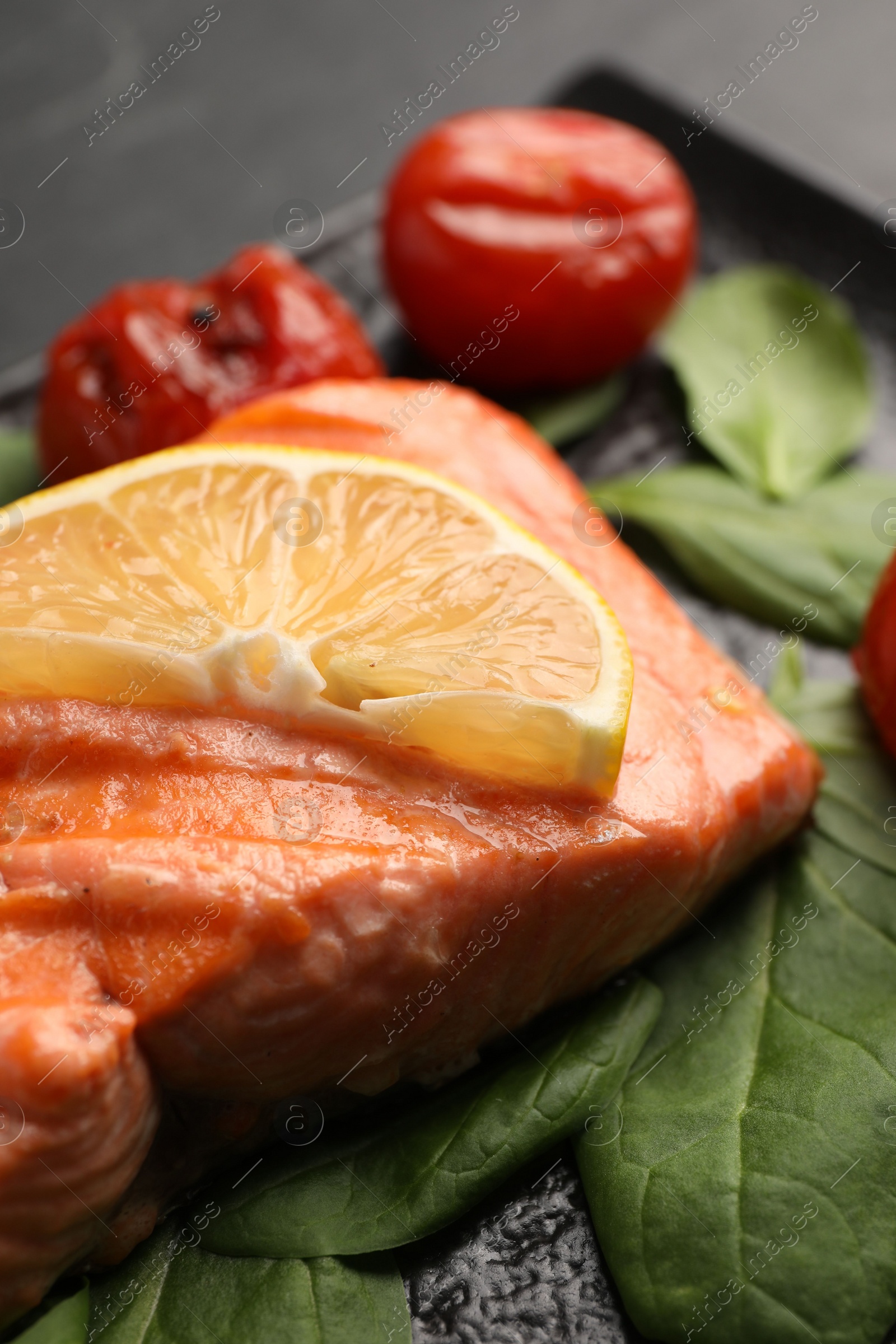 Photo of Tasty grilled salmon with lemon, spinach and tomatoes on table, closeup