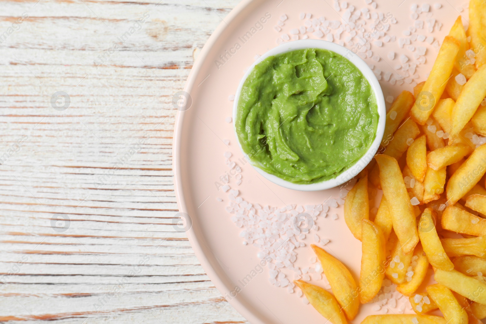 Photo of Plate with french fries and avocado dip on white wooden table, top view. Space for text