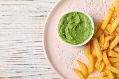 Photo of Plate with french fries and avocado dip on white wooden table, top view. Space for text