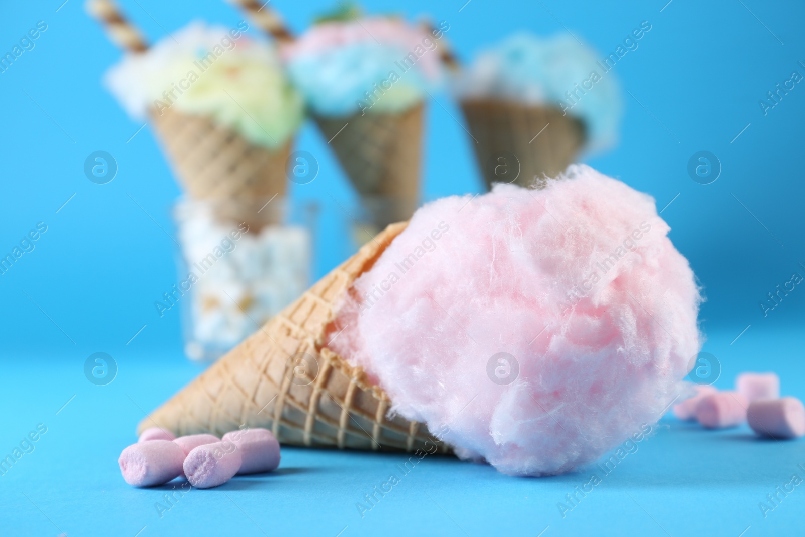 Photo of Sweet cotton candy in waffle cone and marshmallows on light blue background, closeup