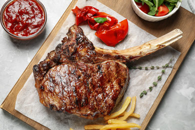 Photo of Delicious grilled ribeye steak served on light grey marble table, flat lay
