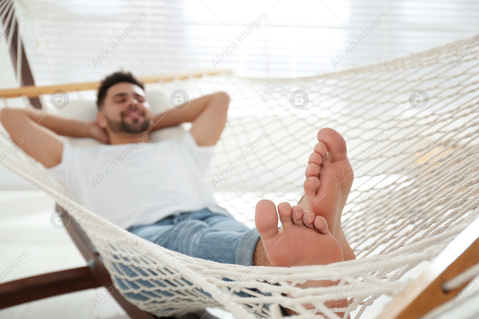 Photo of Young man relaxing in hammock at home, focus on feet