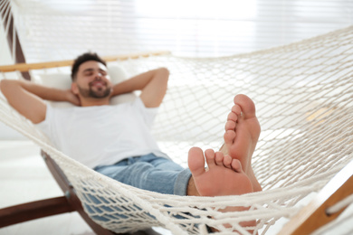 Photo of Young man relaxing in hammock at home, focus on feet