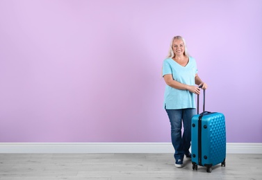 Senior woman with suitcase near color wall. Space for text