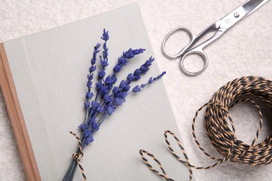 Photo of Preserved lavender flowers, scissors, twine and notebook on white textured table, flat lay