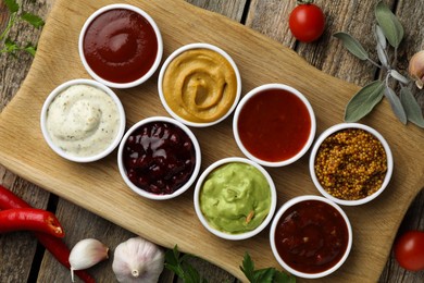 Different tasty sauces in bowls and ingredients on wooden table, top view