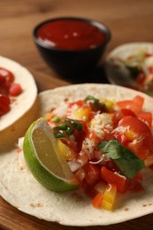 Photo of Delicious taco with vegetables, lime and ketchup on wooden table, closeup