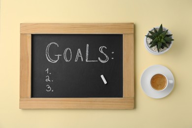 Small blackboard with empty list of goals, houseplant and cup of coffee on beige background, flat lay. Space for text