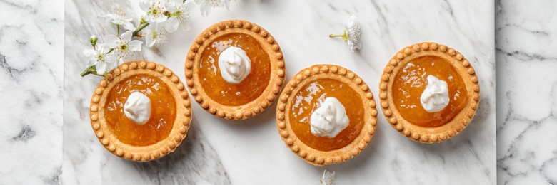 Tasty tartlets with jam on white marble table, top view. Banner design